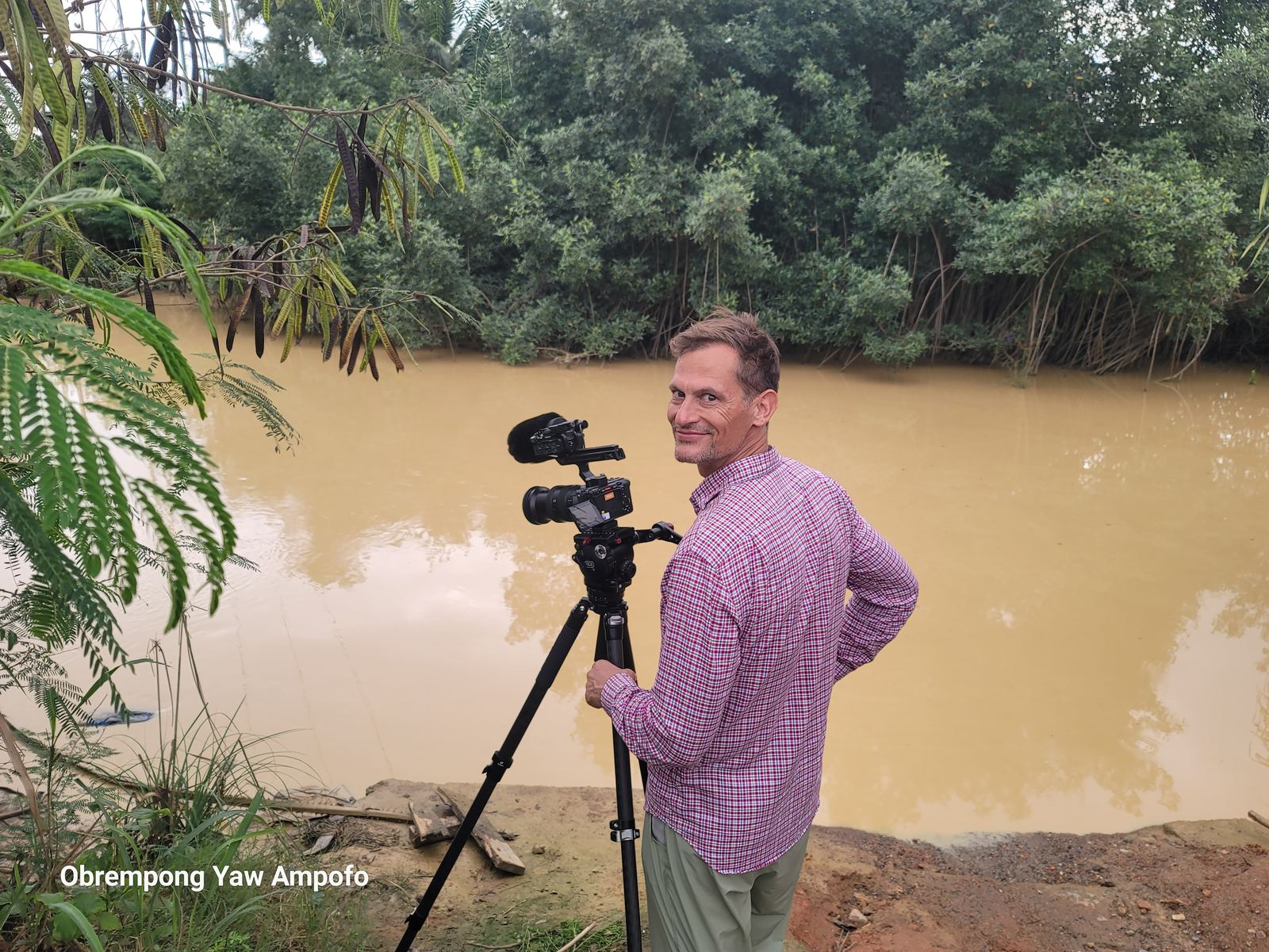 Cameraman filming the muddy Whin River from the riverbank